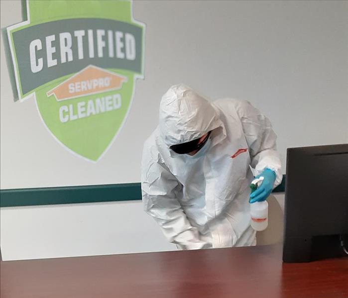 Employee in PPE outfit cleaning an office desk